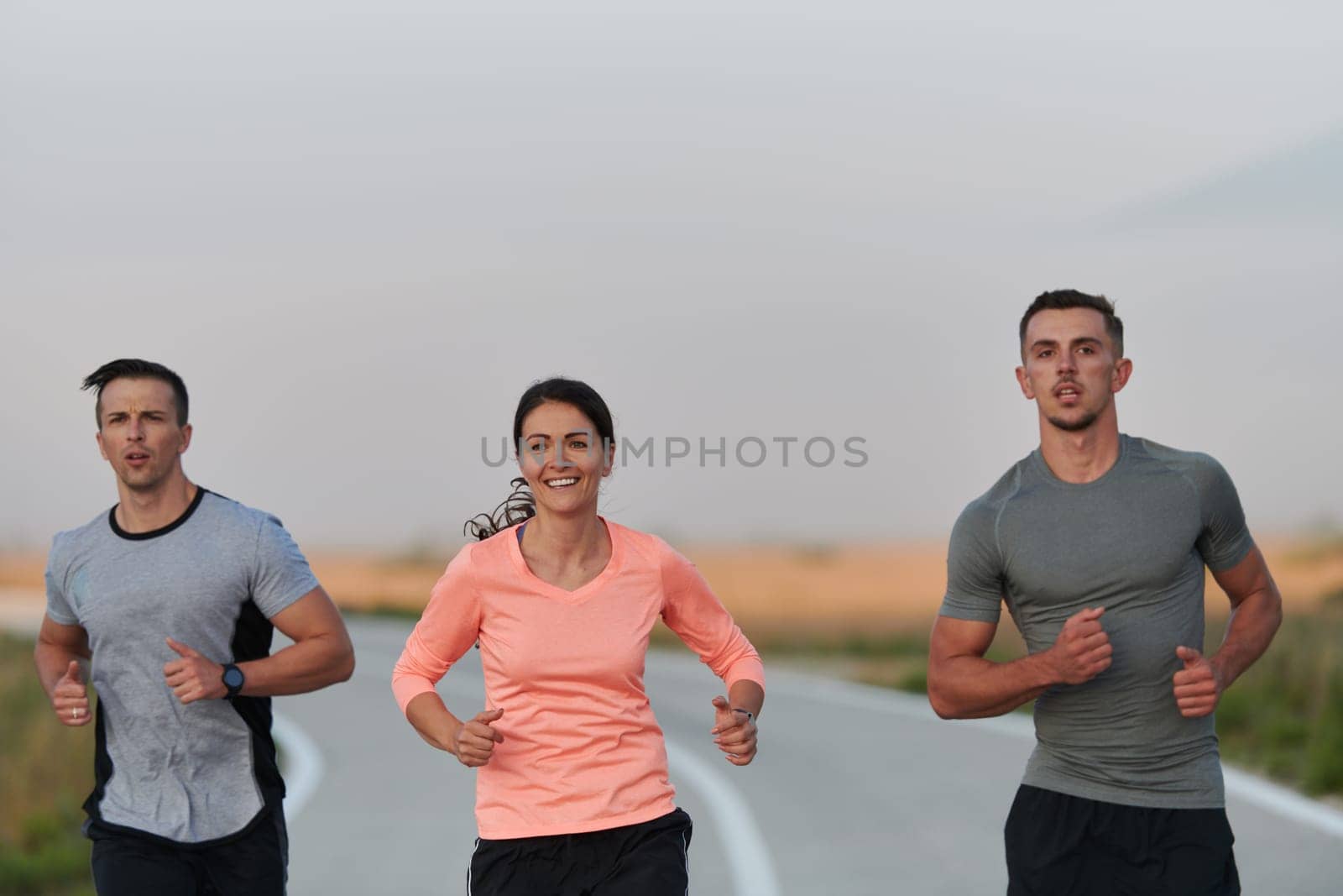 A group of friends, athletes, and joggers embrace the early morning hours as they run through the misty dawn, energized by the rising sun and surrounded by the tranquil beauty of nature.