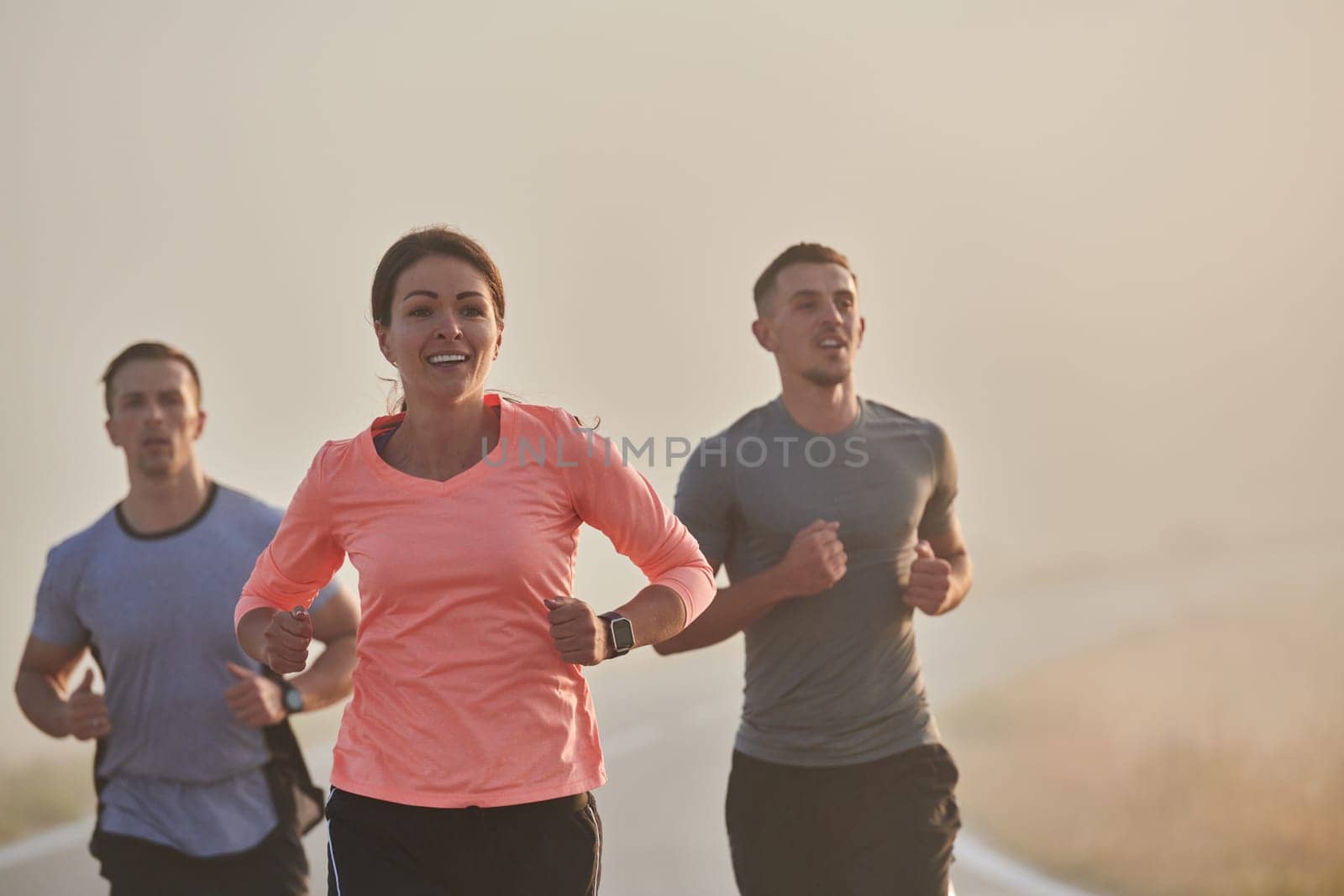 A group of friends, athletes, and joggers embrace the early morning hours as they run through the misty dawn, energized by the rising sun and surrounded by the tranquil beauty of nature.