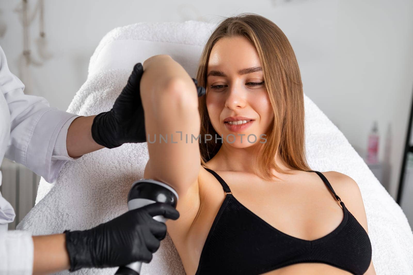 A blonde woman receiving an ultrasound cavitation treatment of her arm at a beauty salon. Body sculpting procedure