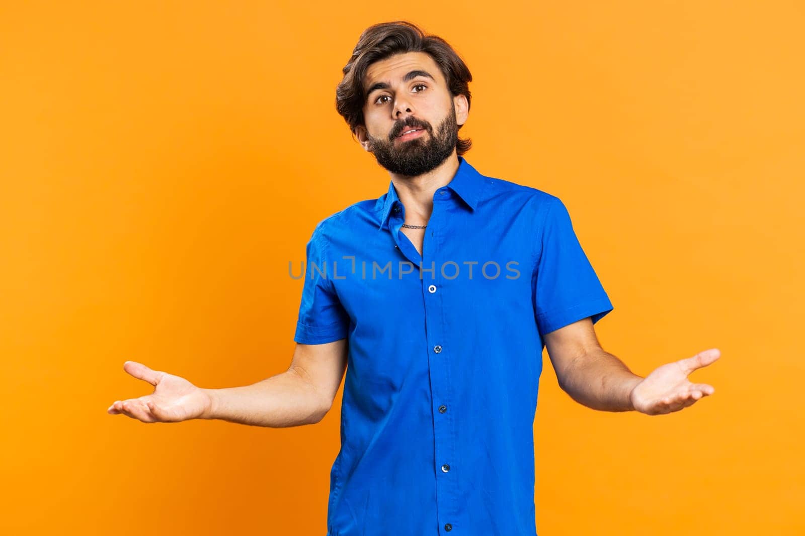 What Why. Sincere irritated man raising hands in indignant expression, ask reason of failure demonstrating disbelief irritation by trouble. Handsome confused middle eastern guy on orange background