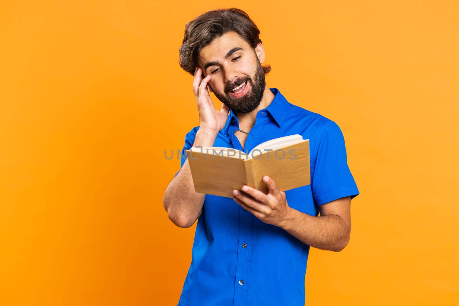 Young excited middle eastern man reading funny interesting fairytale story book, laughing, leisure hobby, knowledge wisdom, education, learning study, wow. Guy isolated on orange studio background