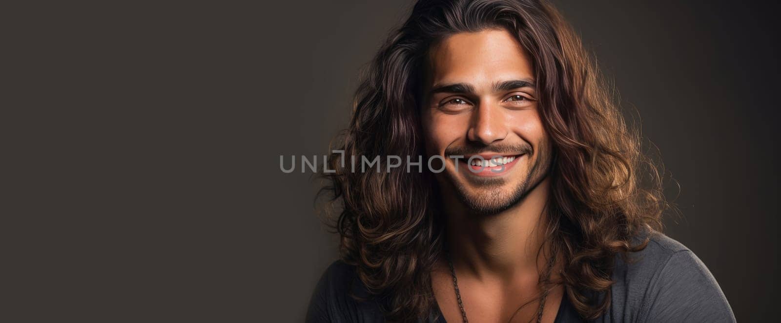 Portrait of an elegant sexy smiling Latino man with perfect skin and long hair, on a gray background. Advertising of cosmetic products, spa treatments shampoos and hair care products, dentistry and medicine, perfumes and cosmetology for men