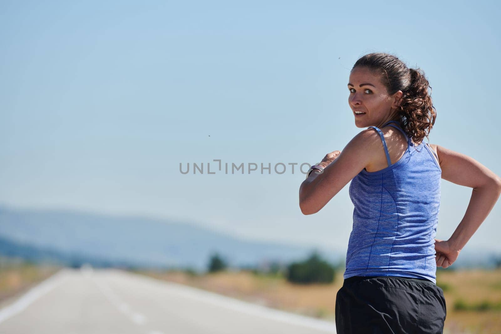 An athletic woman finds freedom and joy in a healthy lifestyle, running through a beautiful road trail at sunrise.