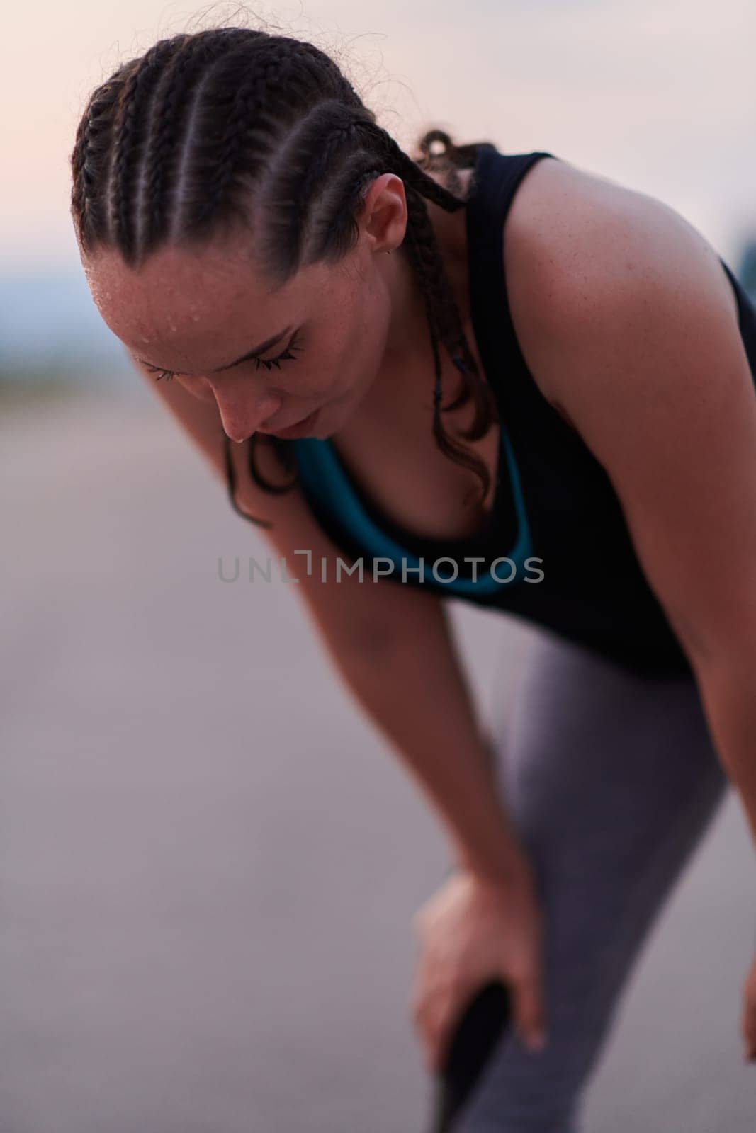 A close-up captures the raw dedication of a female athlete as she rests, sweat glistening, after a rigorous running session, embodying the true spirit of perseverance and commitment to her fitness journey