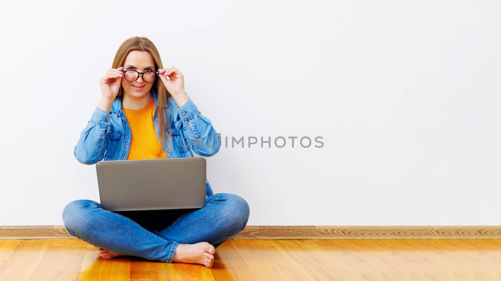 Woman sitting cross-legged on wooden floor holding laptop. Casual indoor portrait with copy space for design and banner