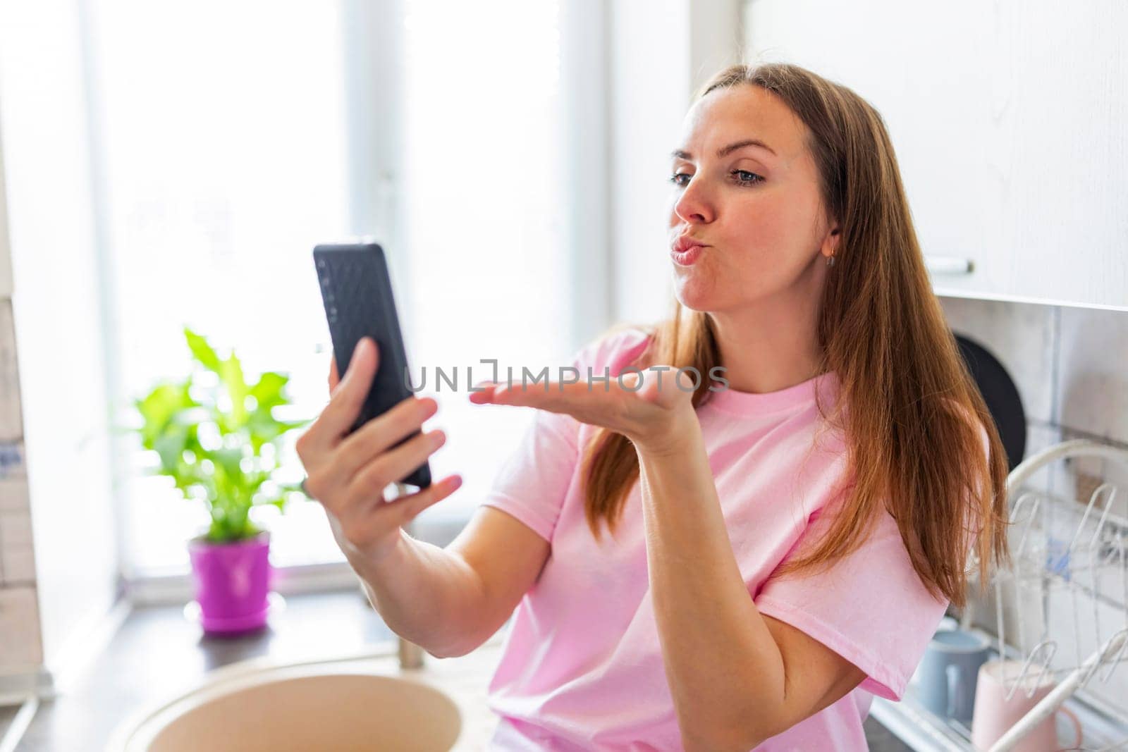 Woman blowing kiss at smartphone for video call. Modern communication and technology concept. Casual home lifestyle with copy space. Design for social media, banner.