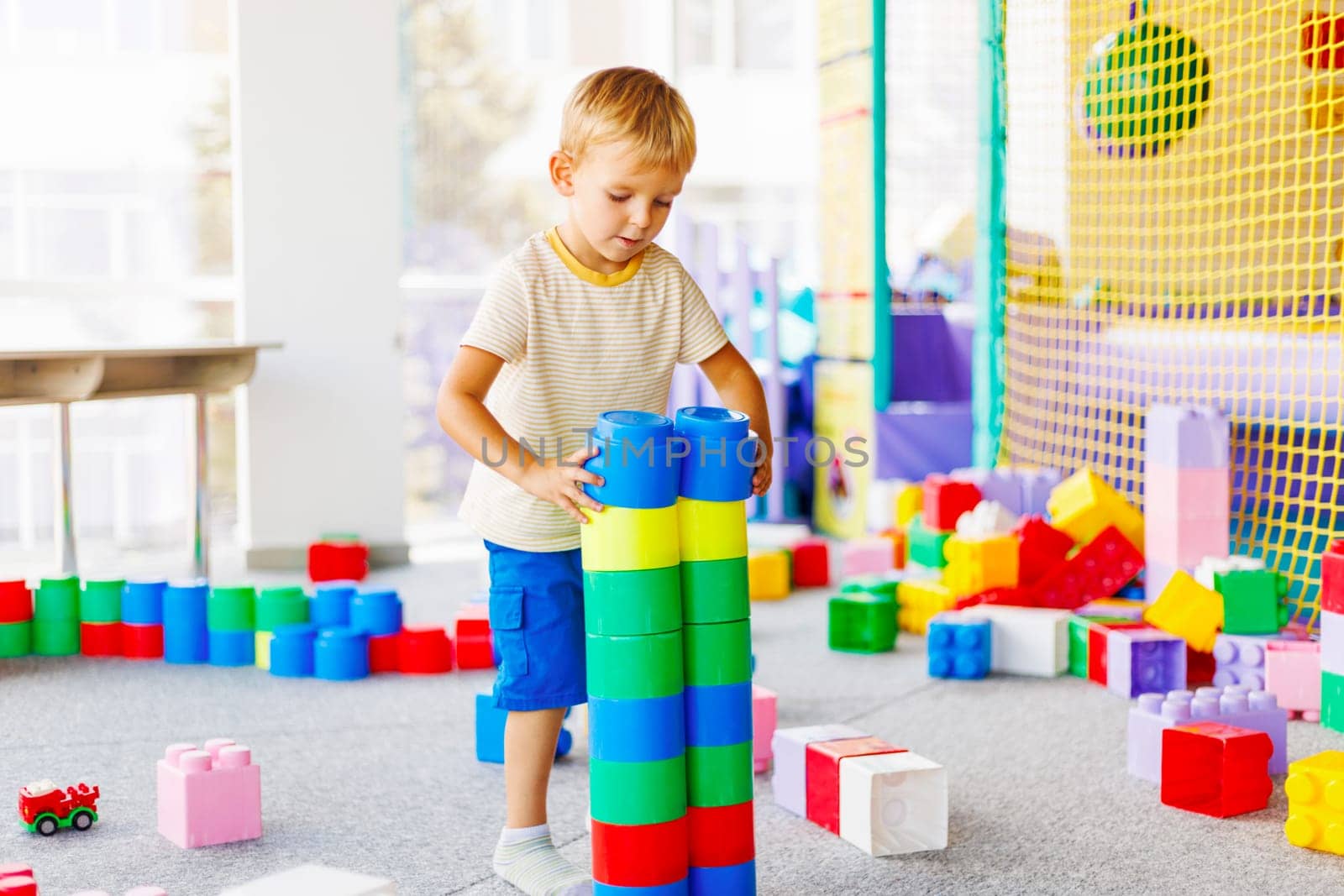 Child playing with colorful building blocks in a playroom setting. Kids' educational toys concept with bright primary colors for design and print