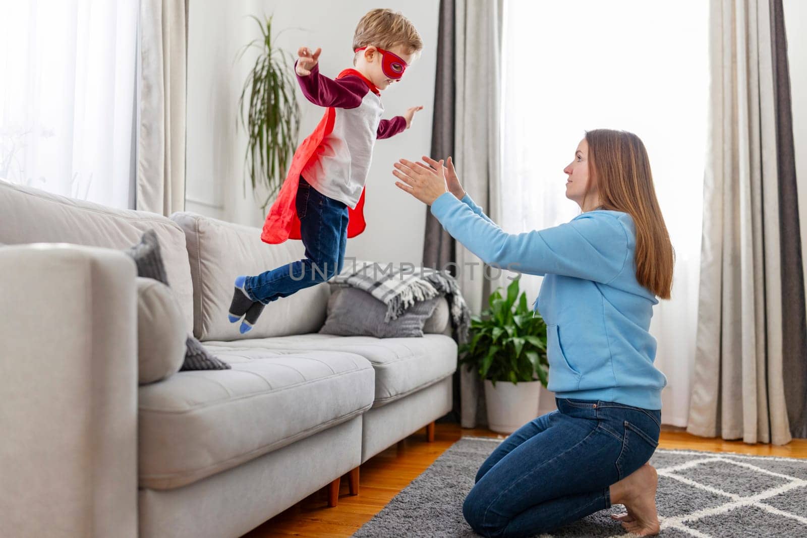 Joyful playtime between a mother and her child pretending to fly like a superhero in a living room.