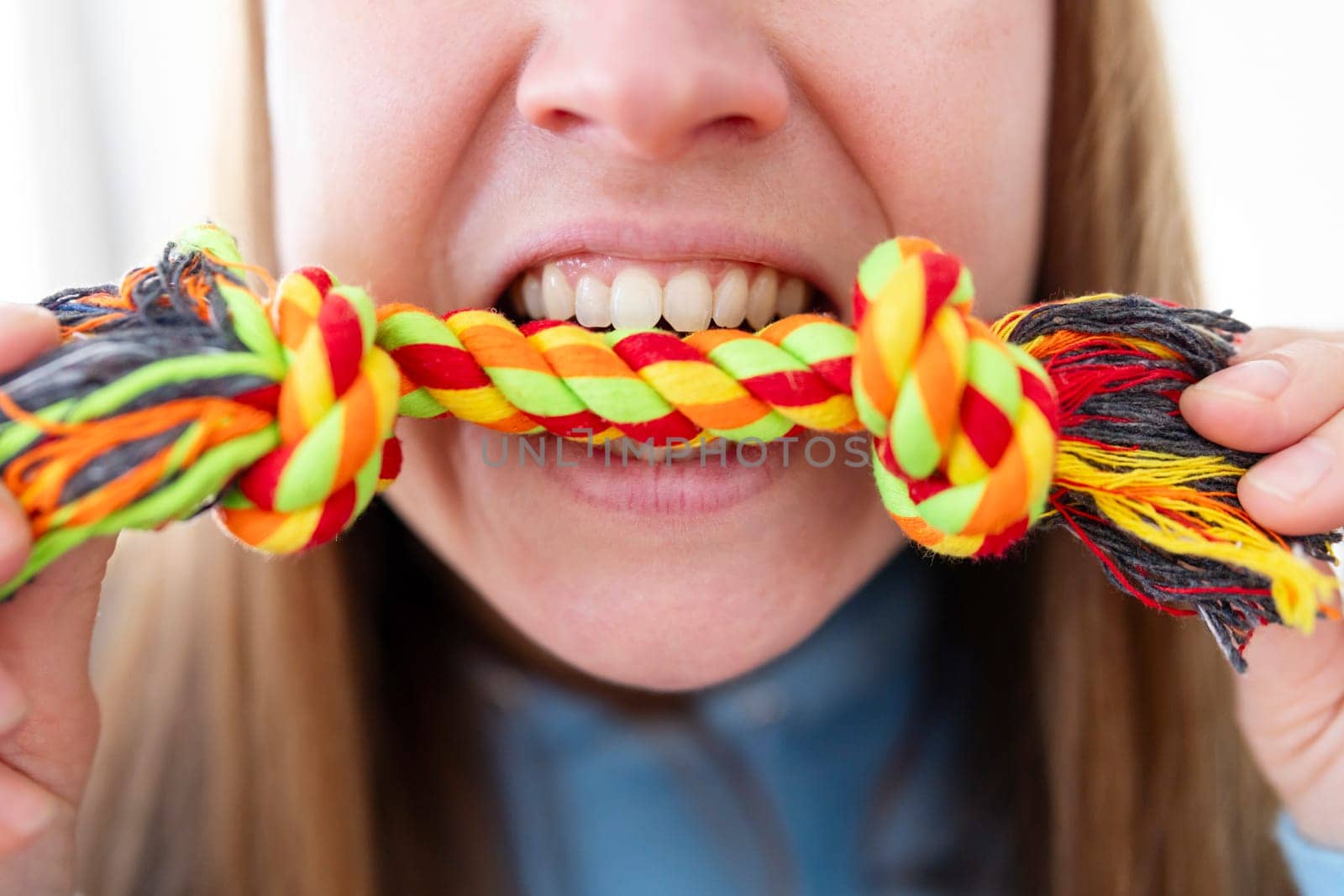 Close-up of a woman's mouth biting a colorful rope toy, depicting playful interaction with a pet.