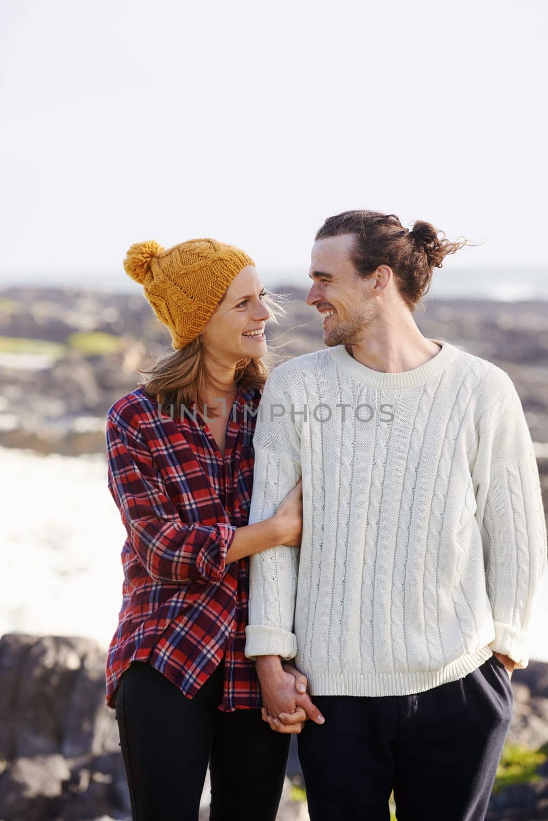 Hug, love and couple by ocean walking in winter for bonding, romantic relationship and relax outdoors. Nature, travel and happy man and woman by seaside for holiday, vacation and weekend together by YuriArcurs