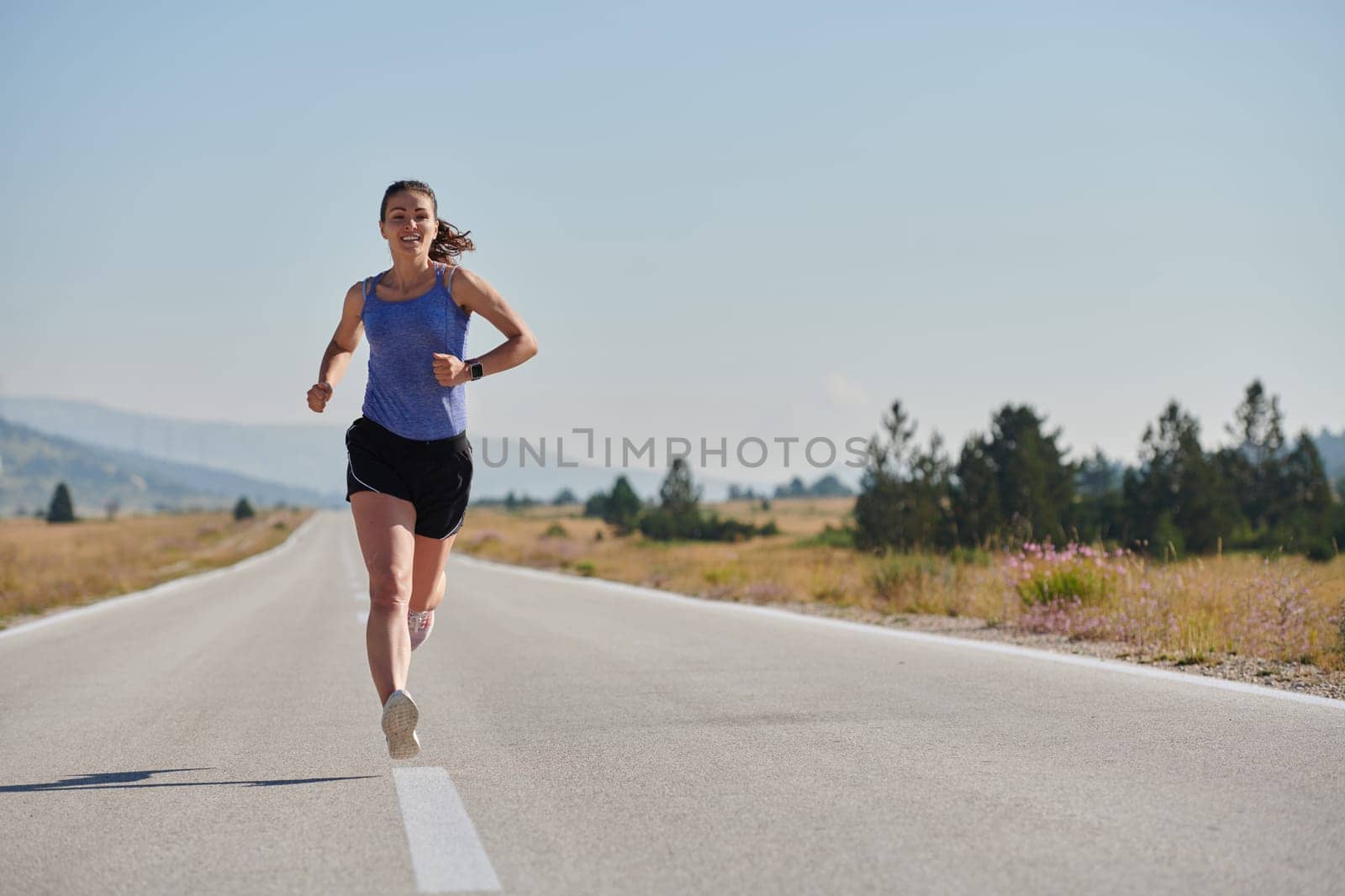 An athletic woman finds freedom and joy in a healthy lifestyle, running through a beautiful road trail at sunrise.