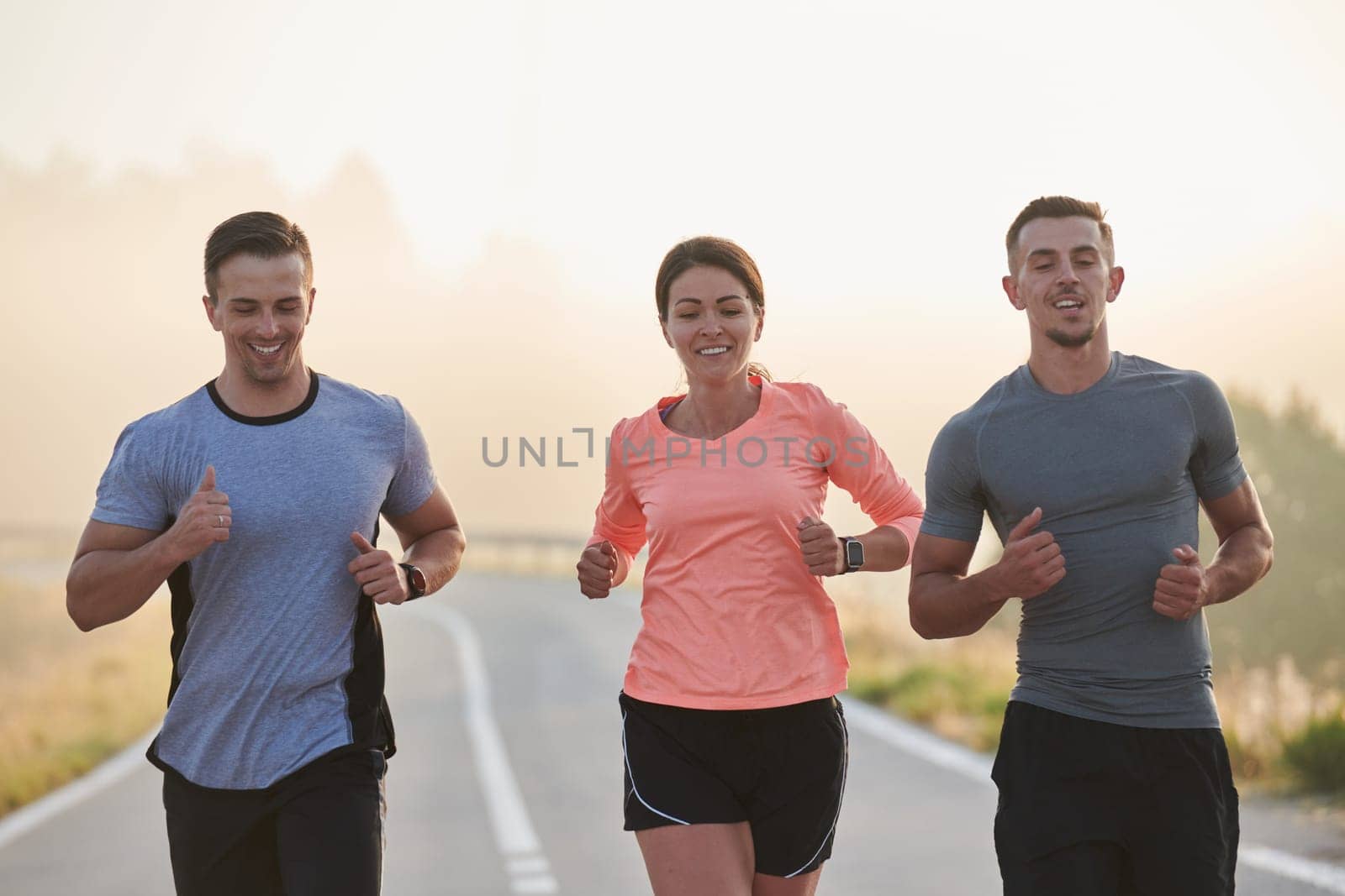 A group of friends, athletes, and joggers embrace the early morning hours as they run through the misty dawn, energized by the rising sun and surrounded by the tranquil beauty of nature.