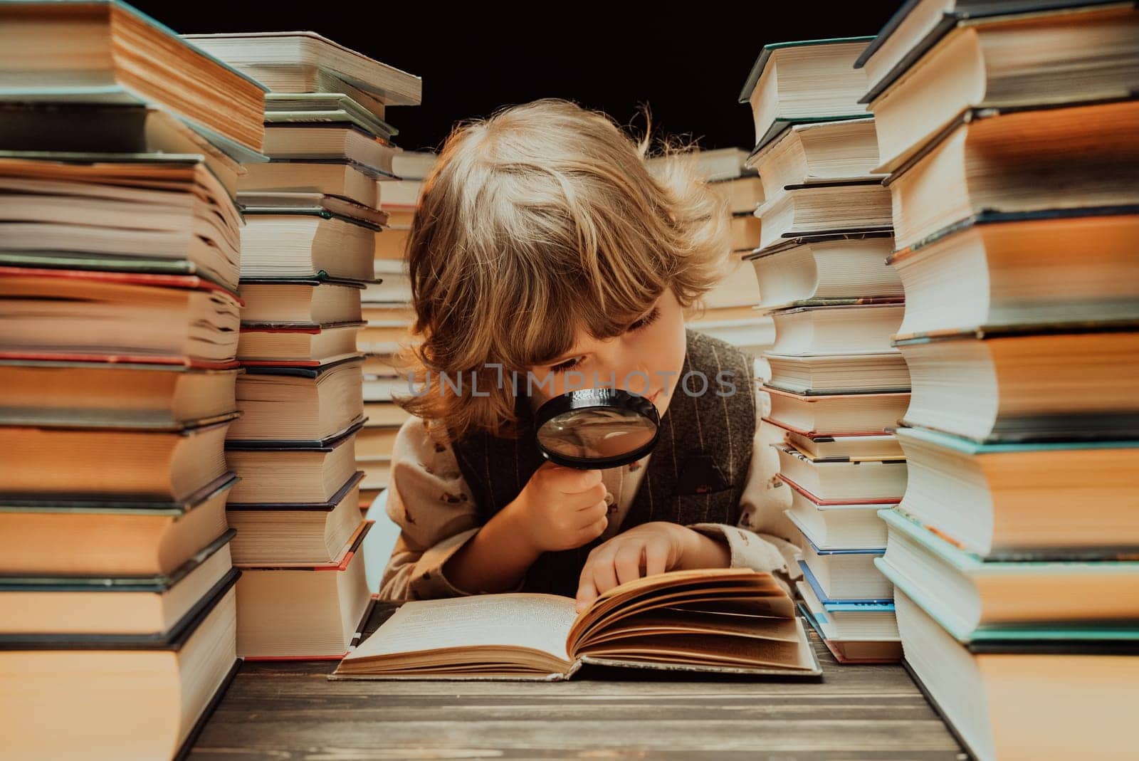 Little researcher boy reads book with magnifying glass in library. Cute clever preschooler playing, studying knowledge with instrument. High quality