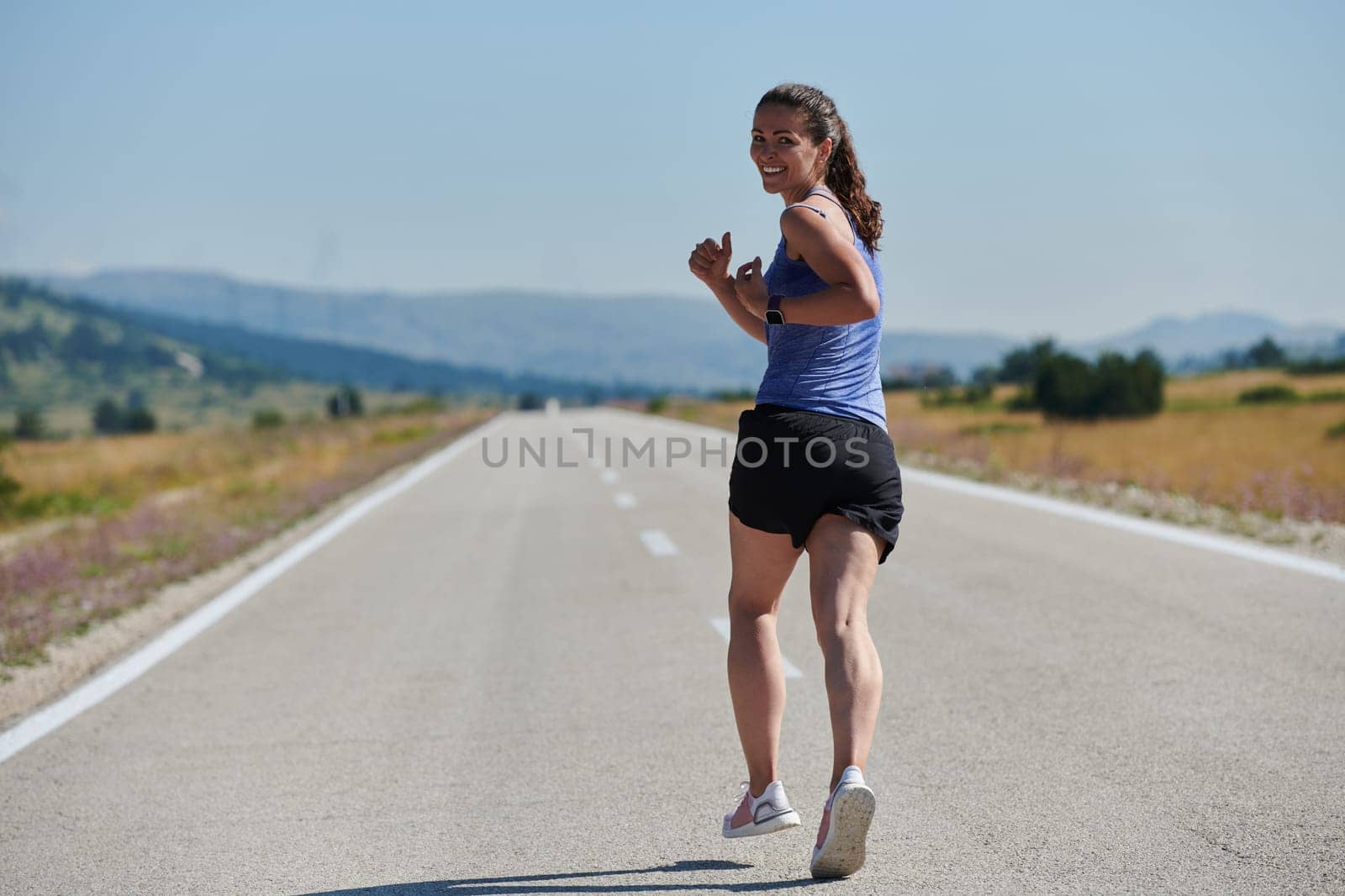 An athletic woman finds freedom and joy in a healthy lifestyle, running through a beautiful road trail at sunrise.