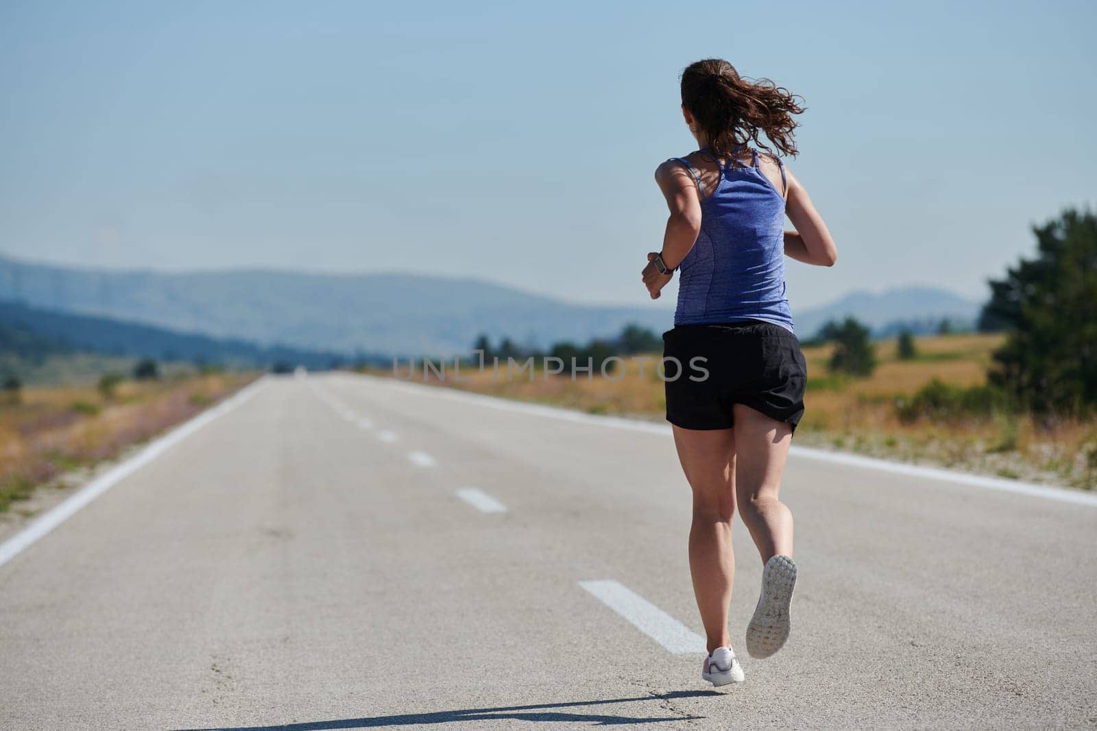 An athletic woman finds freedom and joy in a healthy lifestyle, running through a beautiful road trail at sunrise.