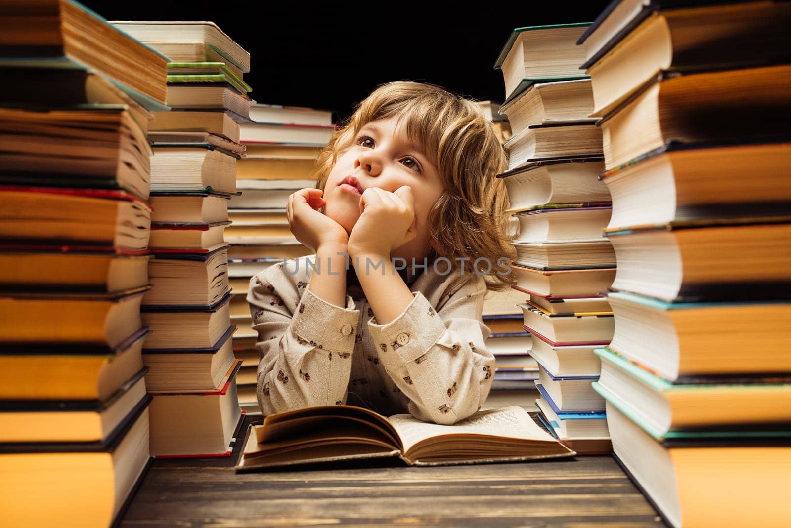 Dreamy little boy sitting at classroom or library desk. Smart child thinking about study or maybe school holidays, end of lesson. High quality