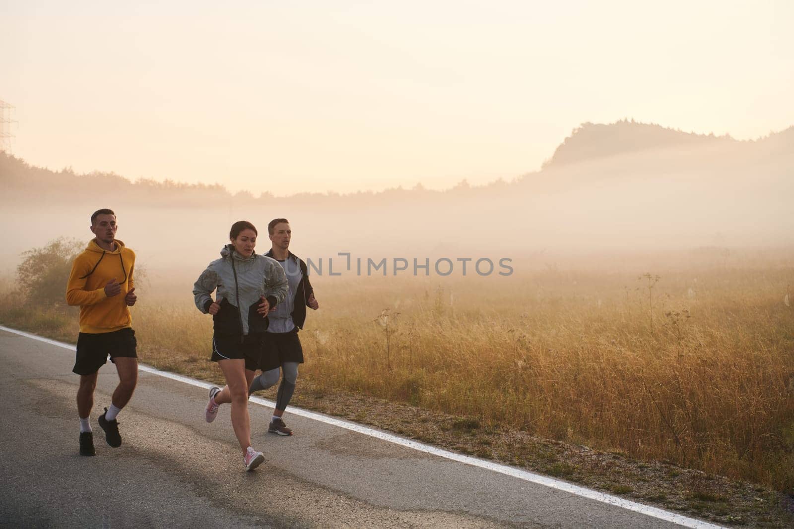 A group of friends, athletes, and joggers embrace the early morning hours as they run through the misty dawn, energized by the rising sun and surrounded by the tranquil beauty of nature.