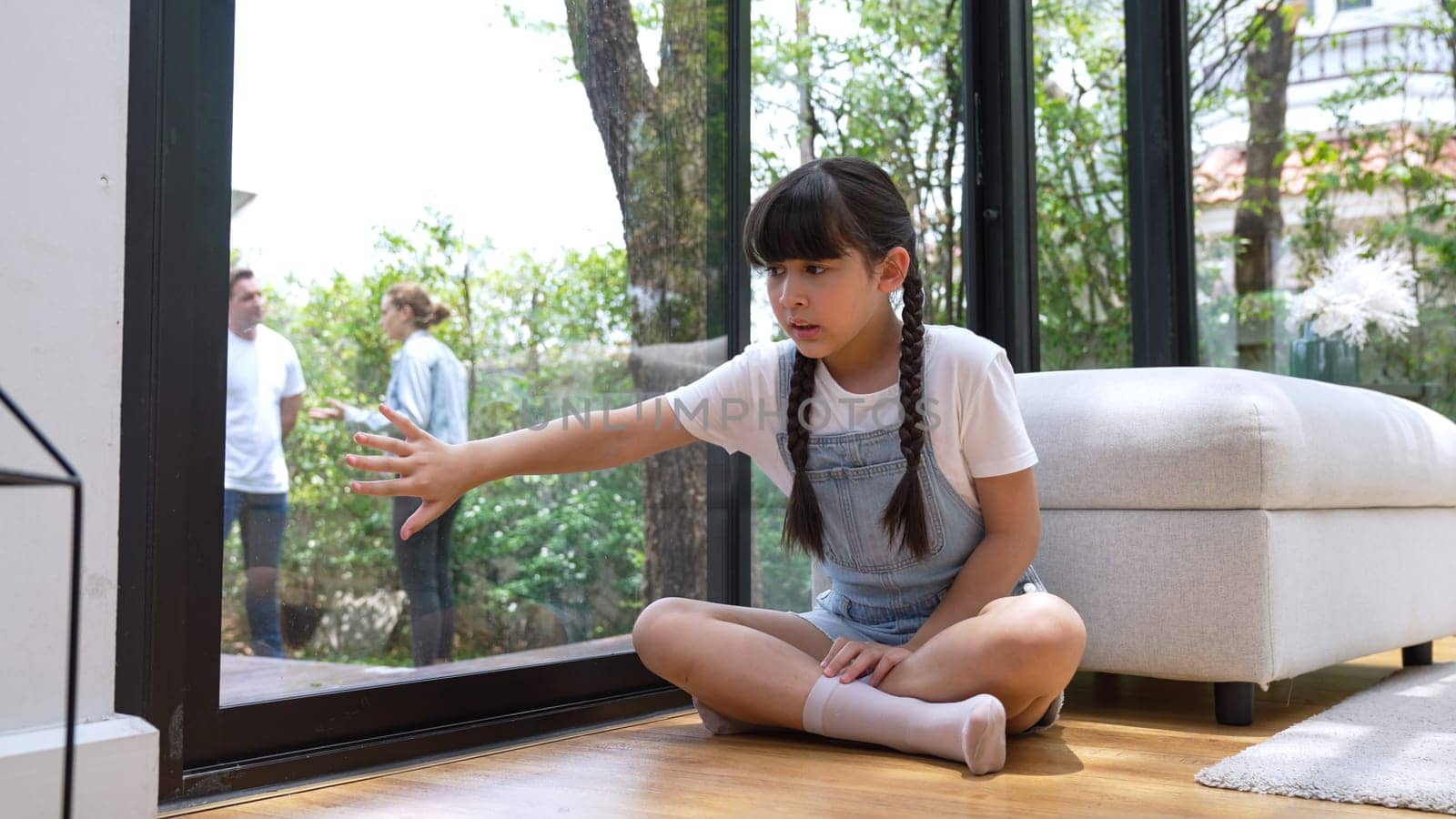 Stressed and unhappy young girl huddle in corner, cover her ears blocking sound of her parent arguing in background. Domestic violence at home and traumatic childhood develop to depression. Synchronos