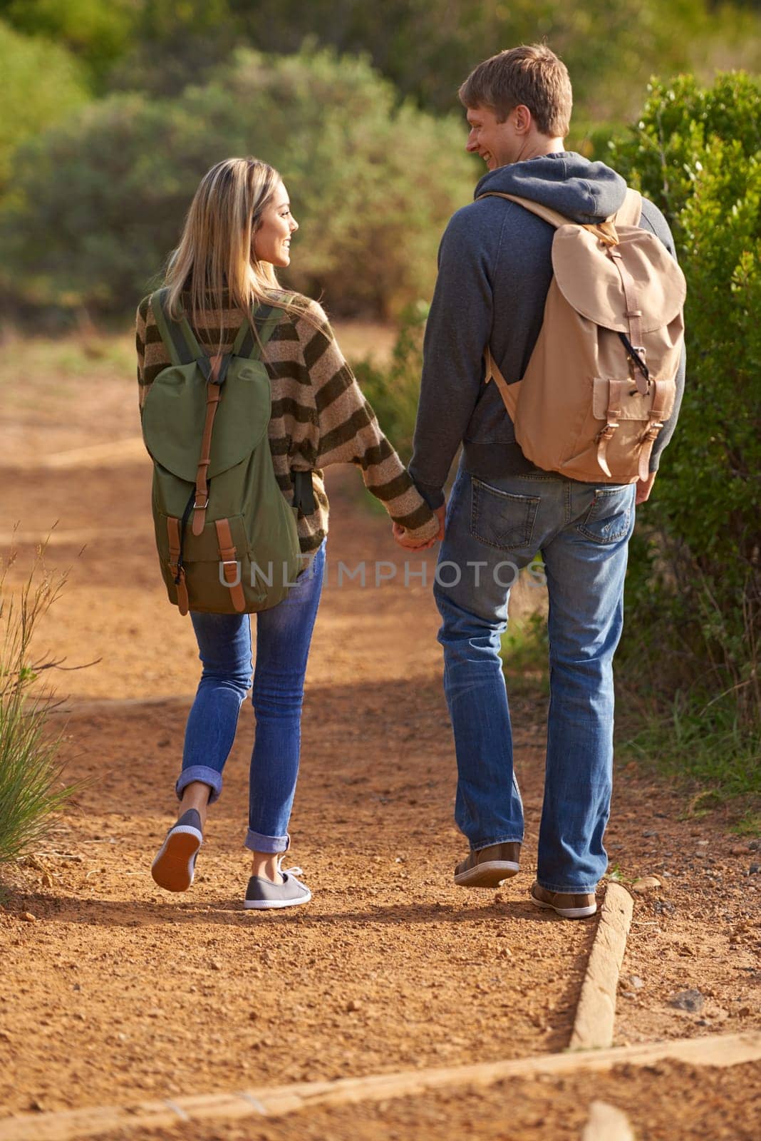 Path, hiking and happy couple holding hands in nature for holiday, travel or adventure outdoor with backpack. Rear view, man or woman trekking in the countryside on vacation, journey or date together by YuriArcurs