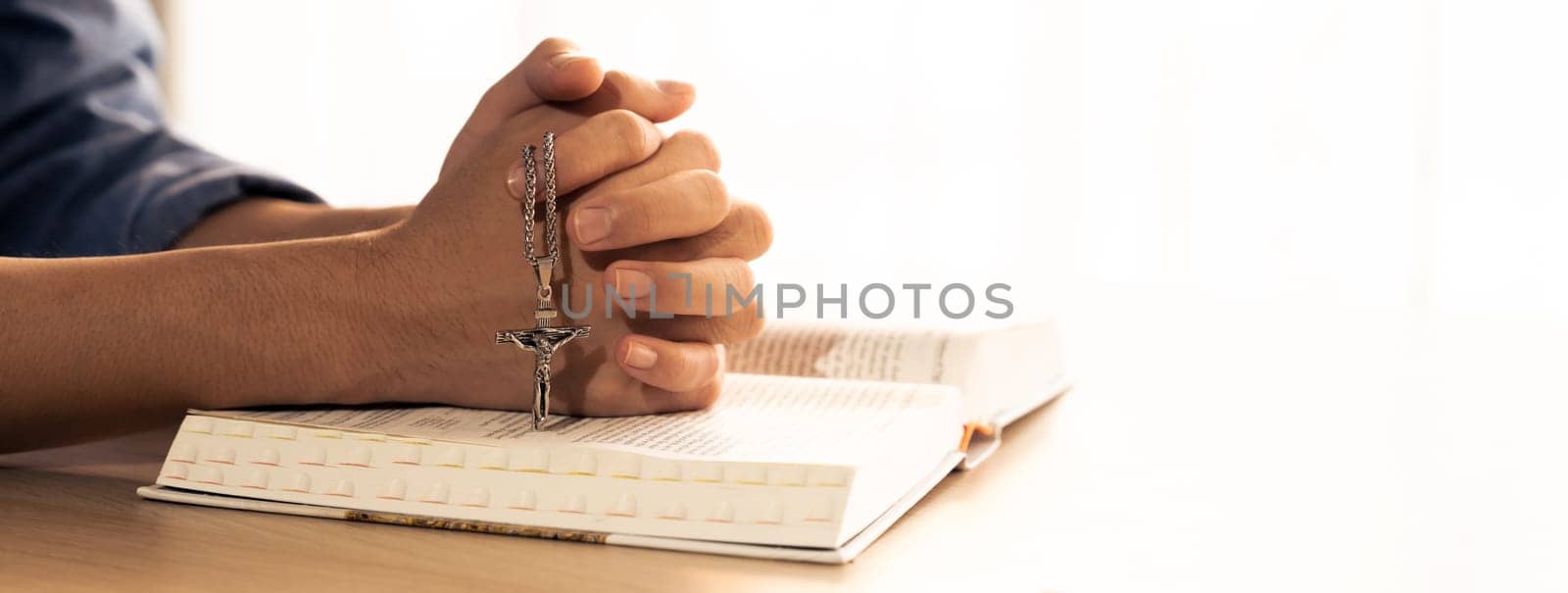 Male folded hand prayed on holy bible book. Blurring background Burgeoning. by biancoblue