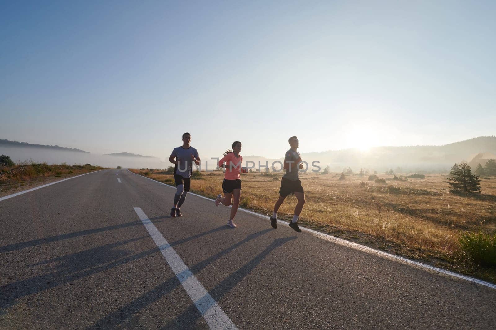 A group of friends, athletes, and joggers embrace the early morning hours as they run through the misty dawn, energized by the rising sun and surrounded by the tranquil beauty of nature by dotshock