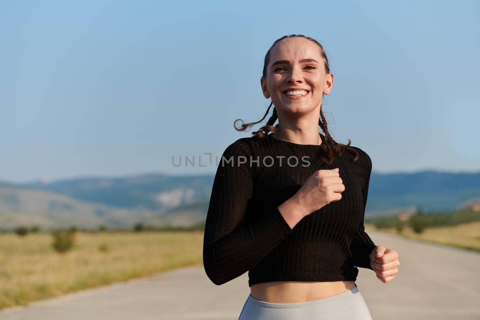 An athletic woman finds freedom and joy in a healthy lifestyle, running through a beautiful road trail at sunrise.