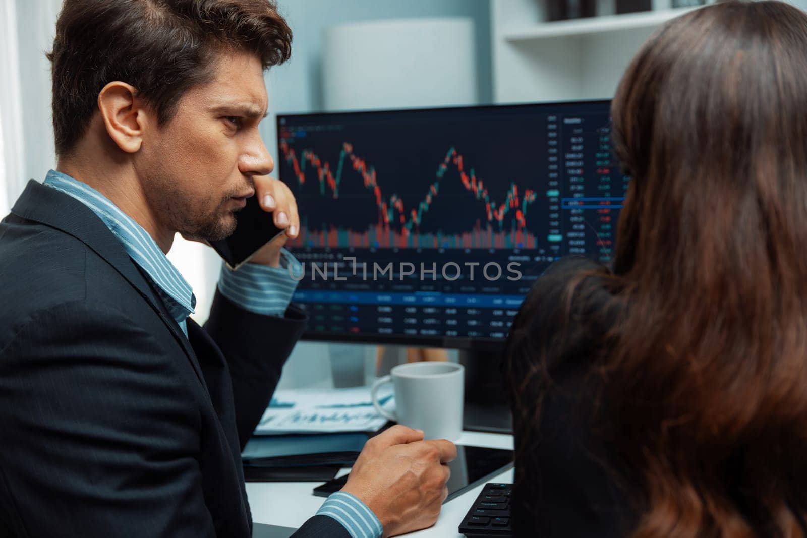 A man broker calling trader businessman to inform high profit point of stock exchange in digital currency while a woman assistance pointing to analyzed data monitor on real time at office. Postulate.