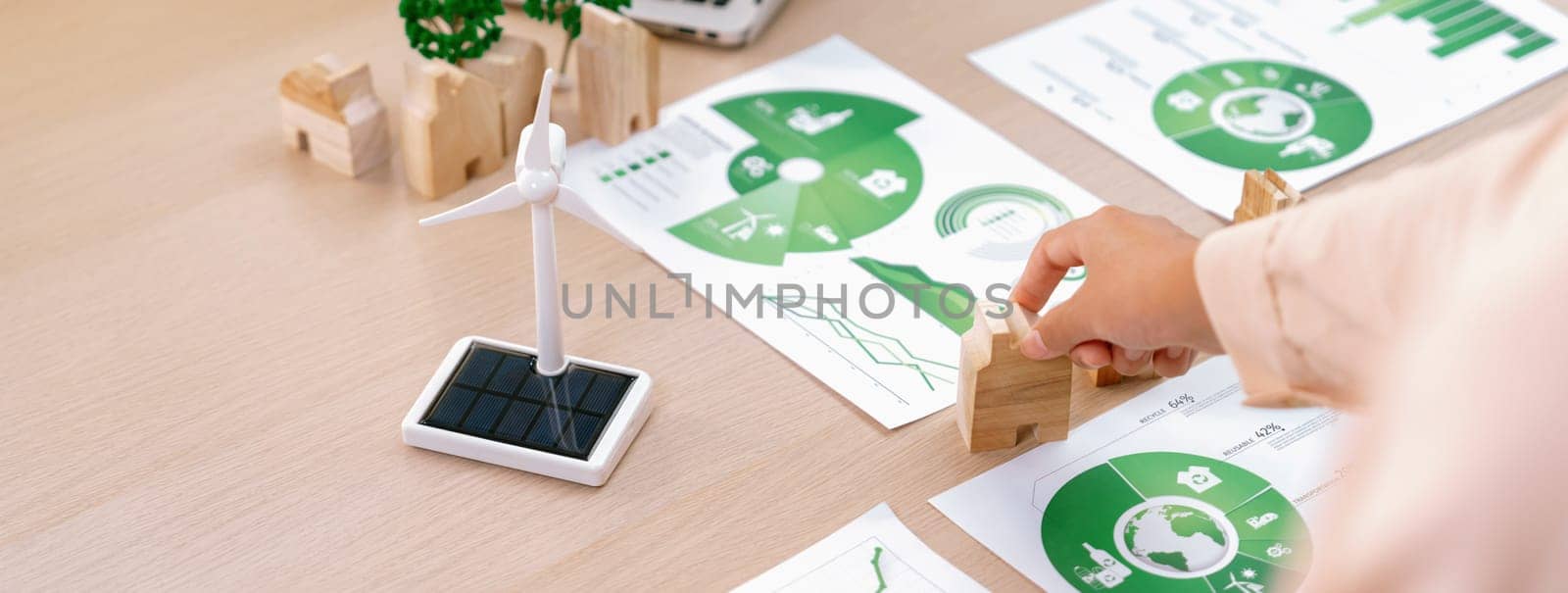 Environmental documents and a windmill model representing the use of clean energy are scattered on the table during a green business discussion about investing in clean energy. Closeup. Delineation.