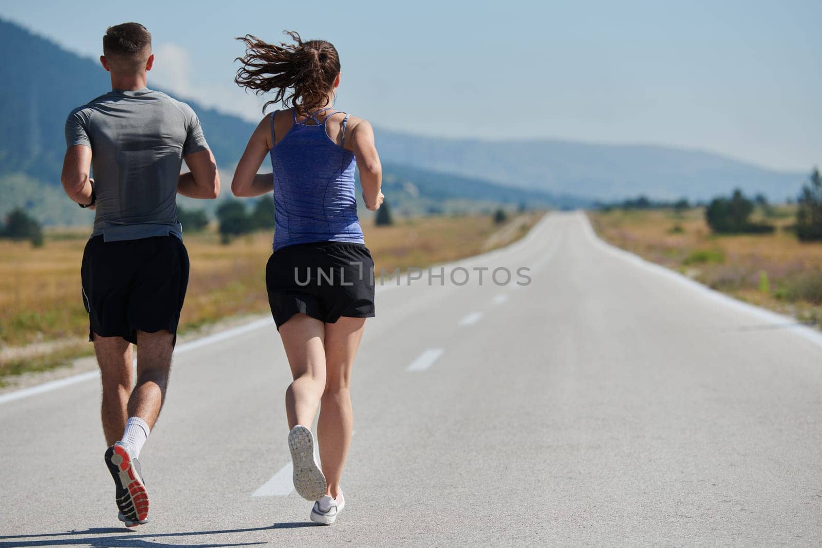 A vibrant couple dashes running the outdoors, embodying the essence of athleticism and romance, their confident strides reflecting a shared commitment to fitness and preparation for future marathon challenges.