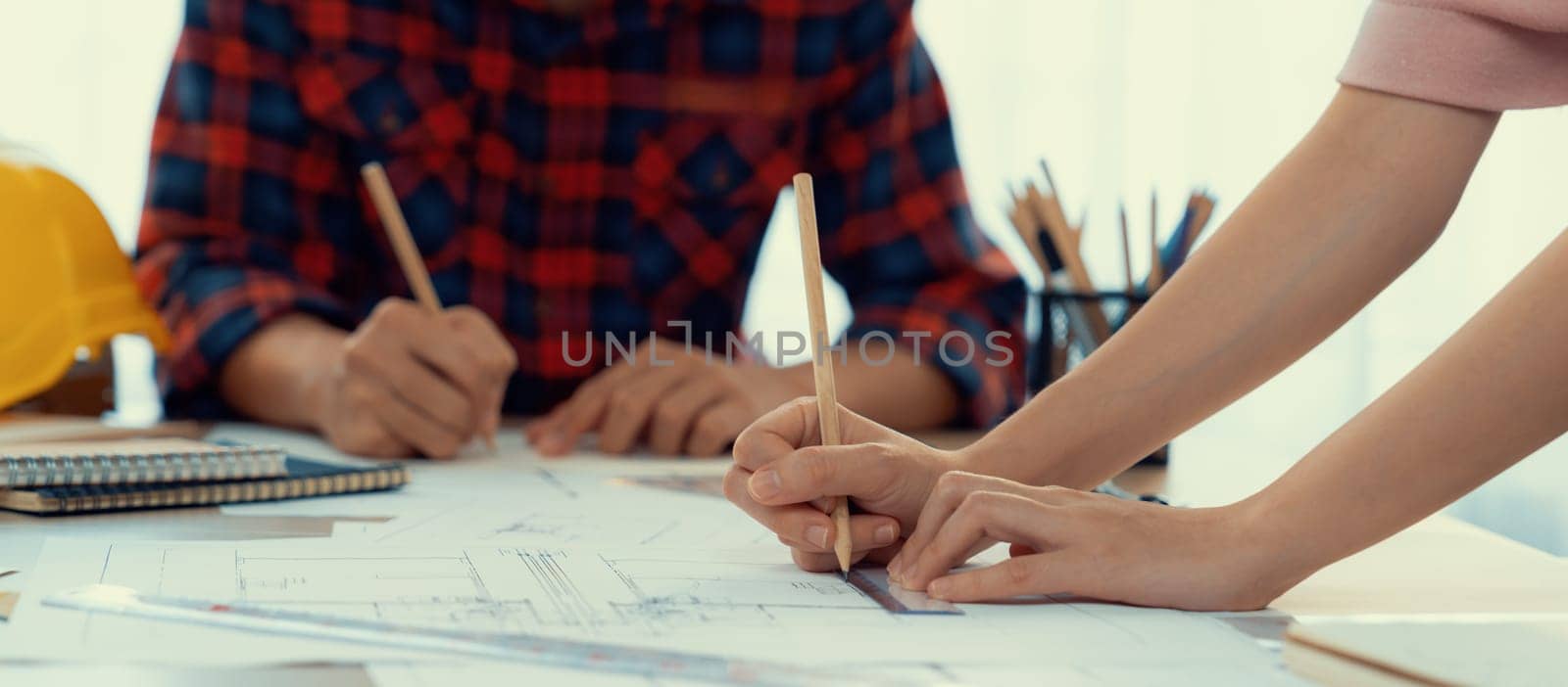 Cropped image of cooperative architect team decide and work together on meeting table with house model, safety helmet and architectural plan scatter around. Closeup. Focus on hand. Burgeoning.