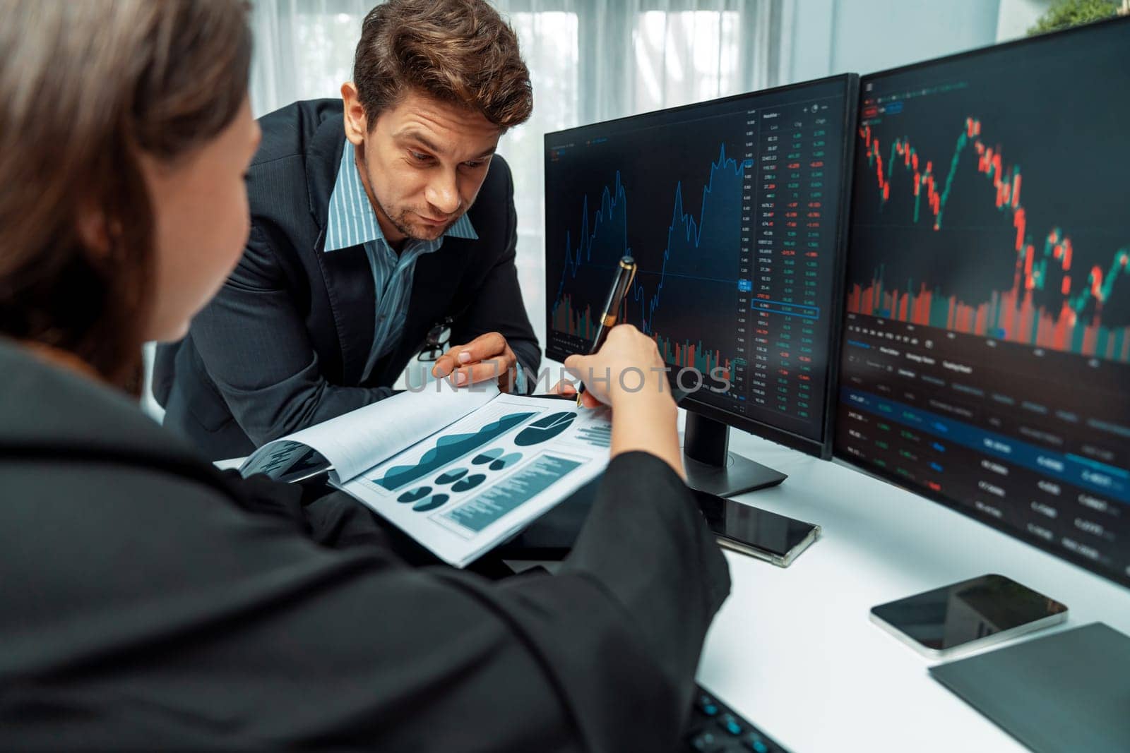 Two business traders discussing value business statistic graph company on paper report analyzing with dynamic stock exchange market currency real time website surround pc screens at office. Postulate.