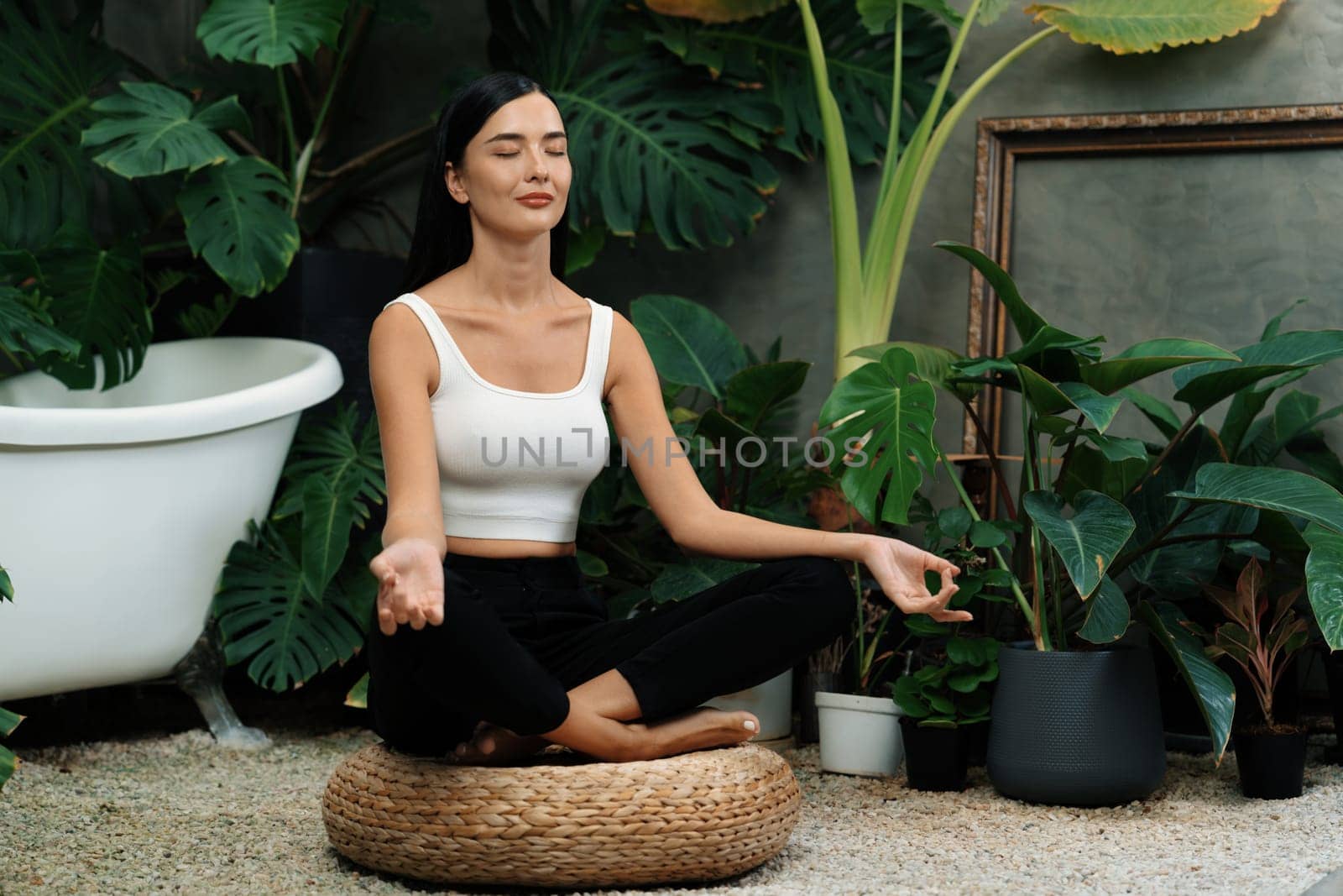 Young woman doing morning yoga and meditation in natural garden with plant leaf, enjoying the solitude and practicing meditative poses. Mindfulness activity and healthy mind lifestyle. Blithe