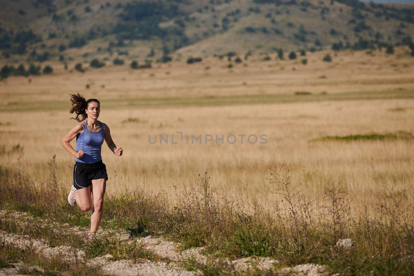 An athletic woman finds freedom and joy in a healthy lifestyle, running through a beautiful road trail at sunrise.