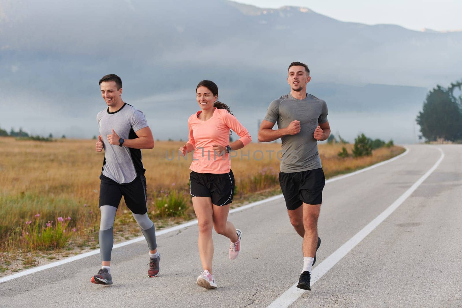 A group of friends, athletes, and joggers embrace the early morning hours as they run through the misty dawn, energized by the rising sun and surrounded by the tranquil beauty of nature.