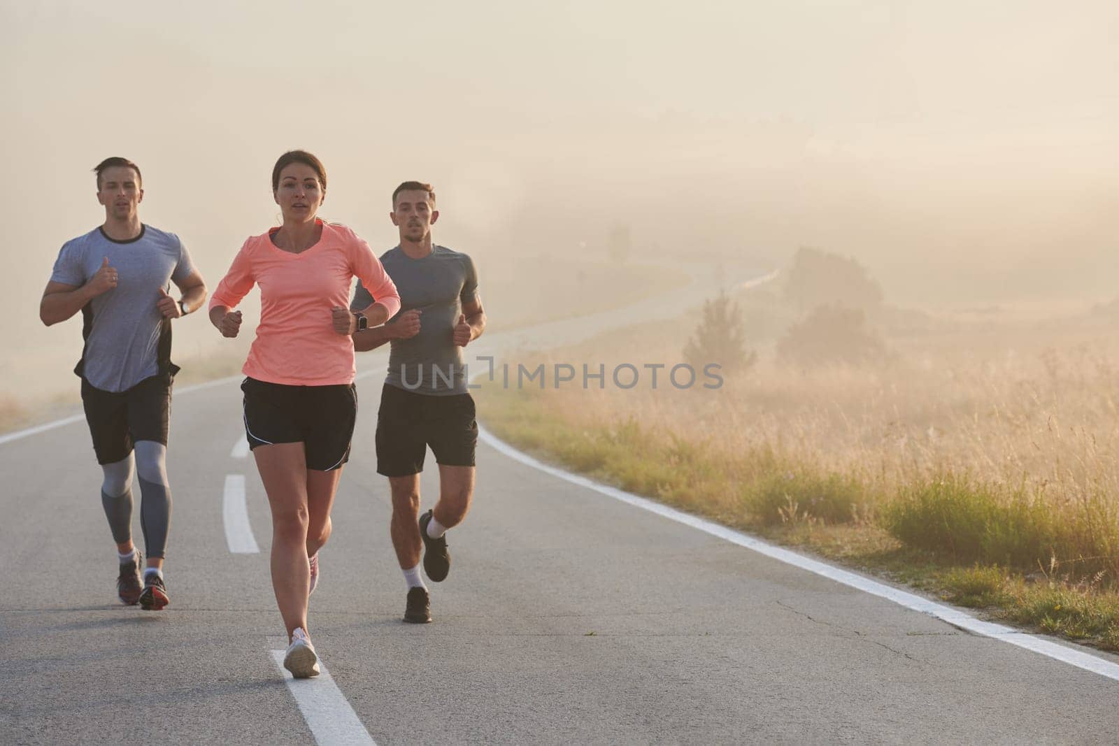 A group of friends, athletes, and joggers embrace the early morning hours as they run through the misty dawn, energized by the rising sun and surrounded by the tranquil beauty of nature.