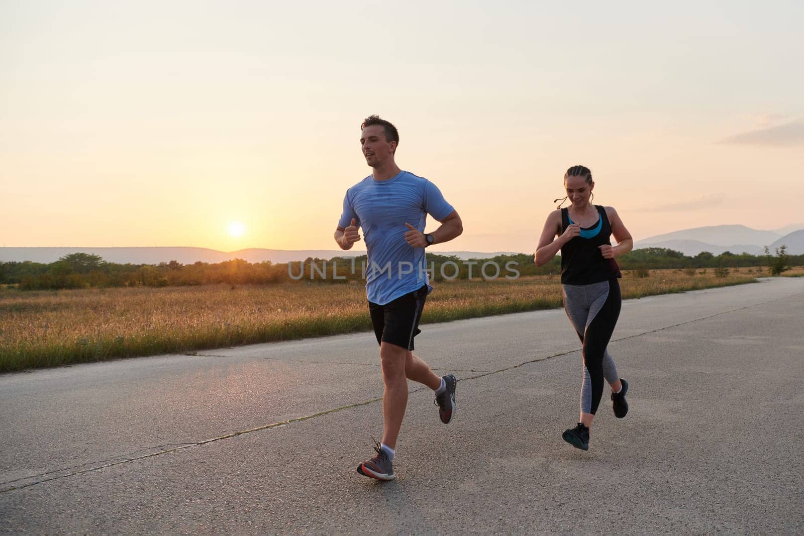 A vibrant couple dashes running the outdoors, embodying the essence of athleticism and romance, their confident strides reflecting a shared commitment to fitness and preparation for future marathon challenges.