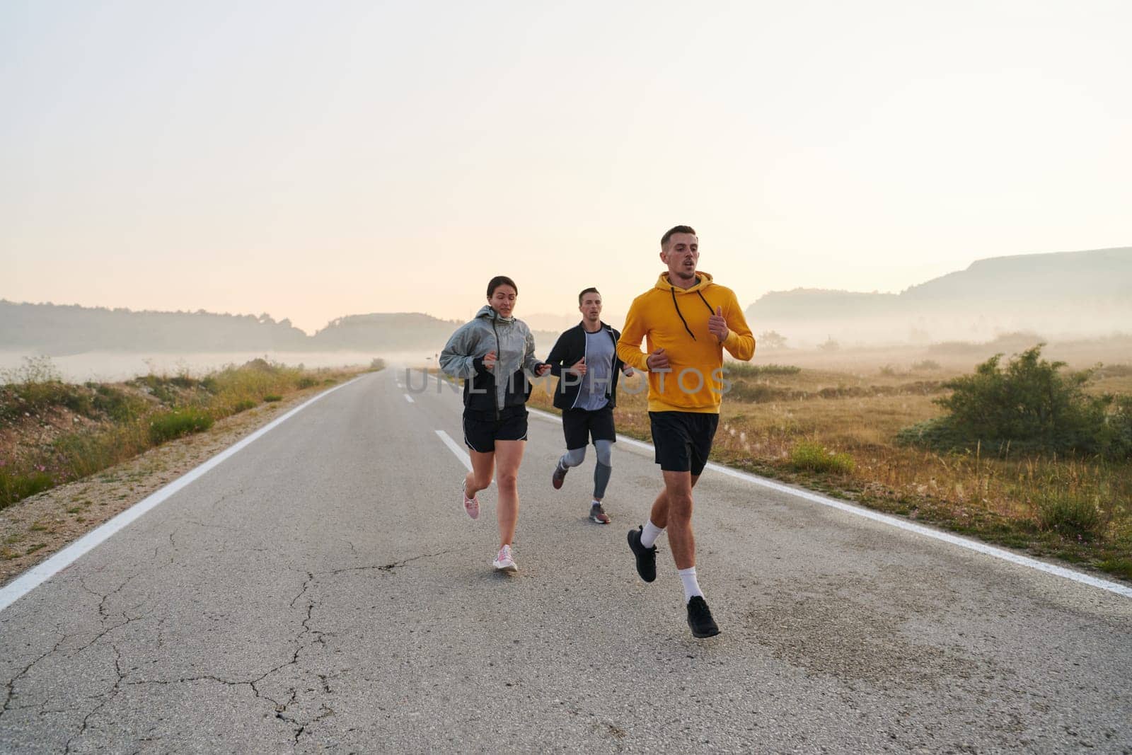 A group of friends, athletes, and joggers embrace the early morning hours as they run through the misty dawn, energized by the rising sun and surrounded by the tranquil beauty of nature.