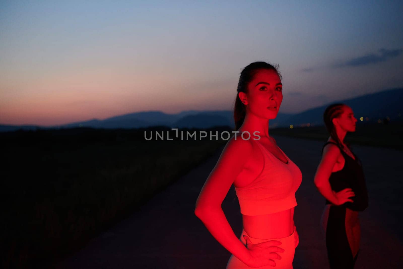 After a grueling nighttime run, an athlete strikes a confident pose, bathed in the red glow of the surroundings, showcasing both exhaustion and determination.