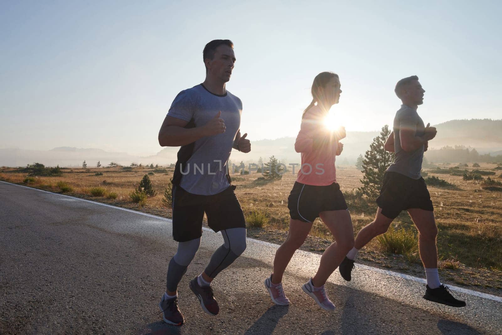 A group of friends, athletes, and joggers embrace the early morning hours as they run through the misty dawn, energized by the rising sun and surrounded by the tranquil beauty of nature.