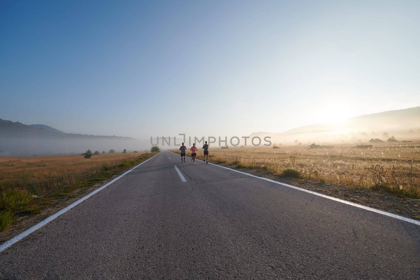 A group of friends, athletes, and joggers embrace the early morning hours as they run through the misty dawn, energized by the rising sun and surrounded by the tranquil beauty of nature by dotshock