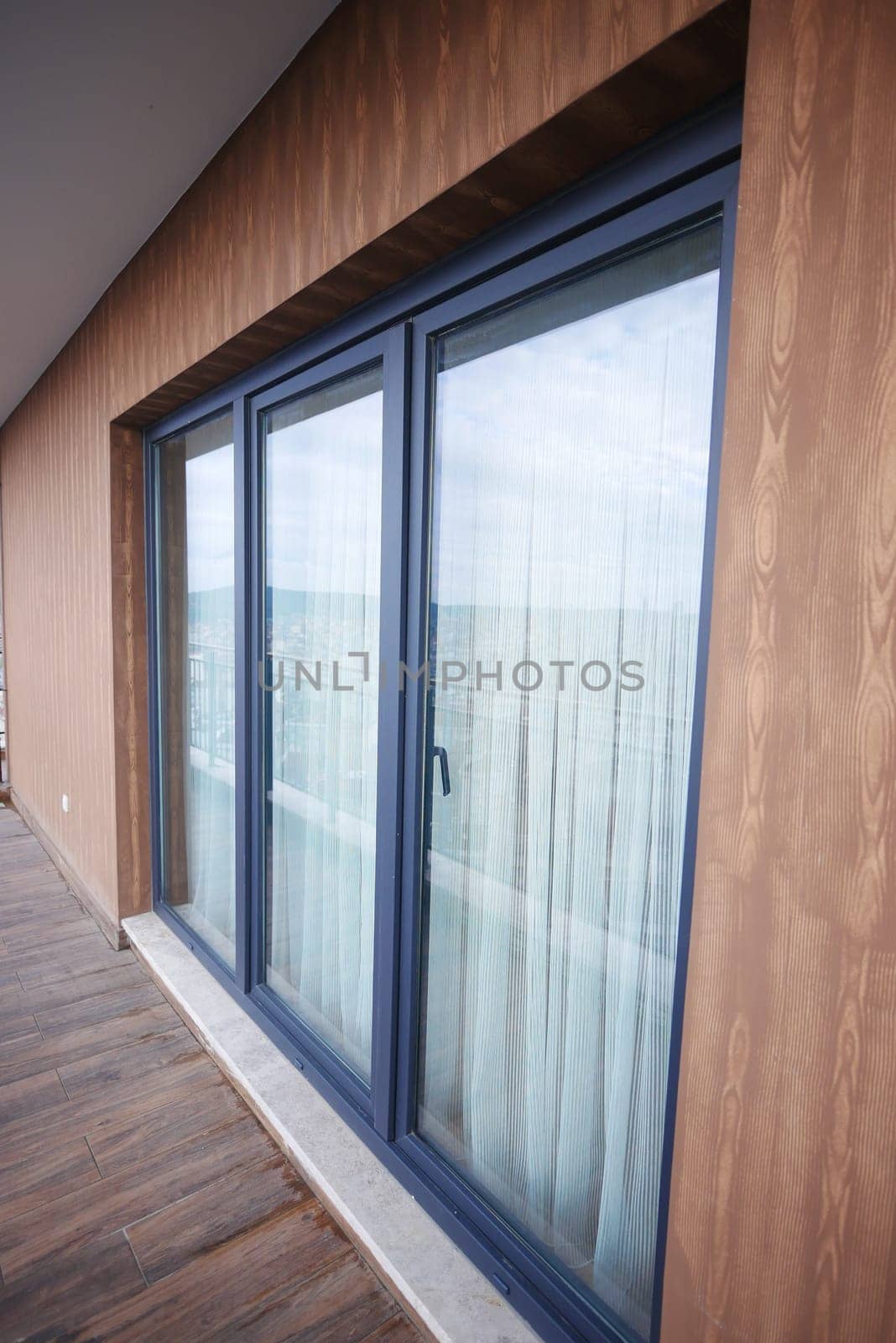 Modern front window with thin curtains and house walls from the outside view..