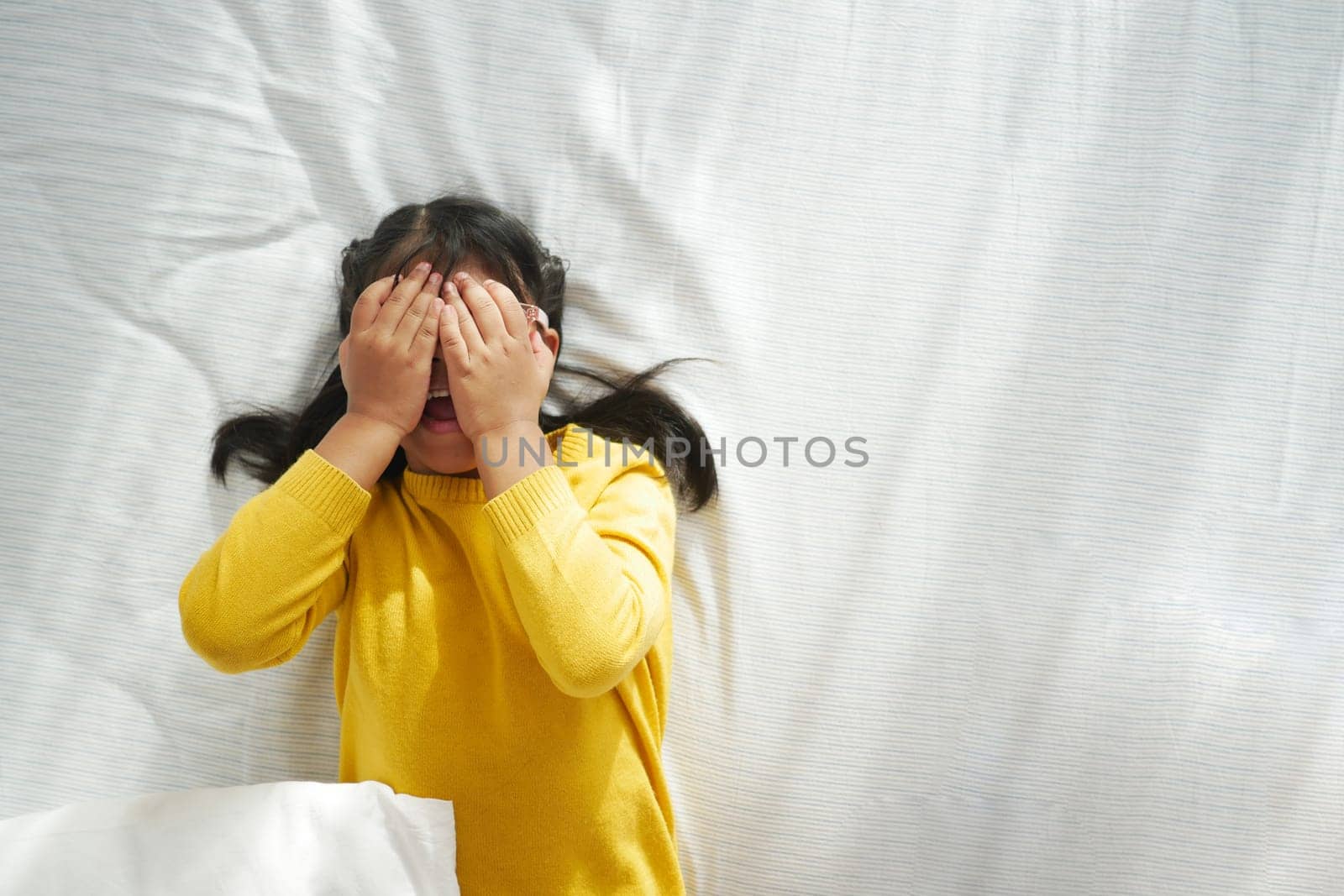 Sad child covered his face with his hands while lying on the bed at home