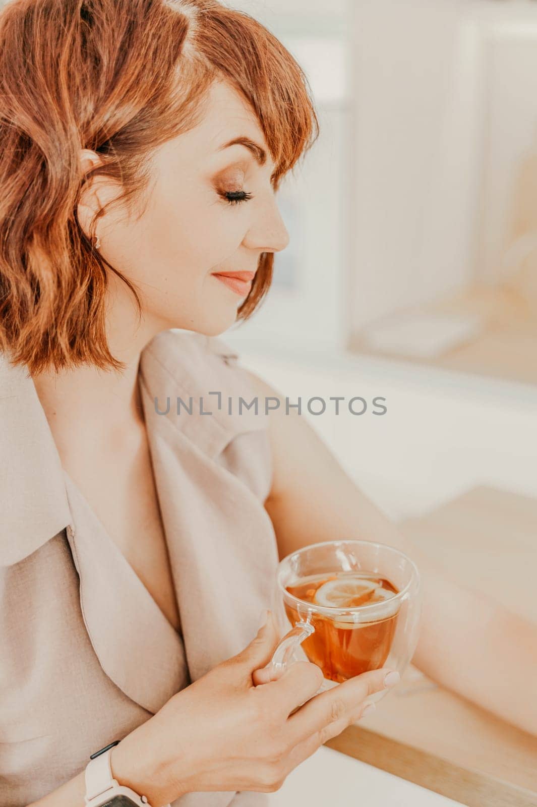 Woman drinks tea close-up. Portrait of a brunette in a beige dress with a transparent mug in her hands