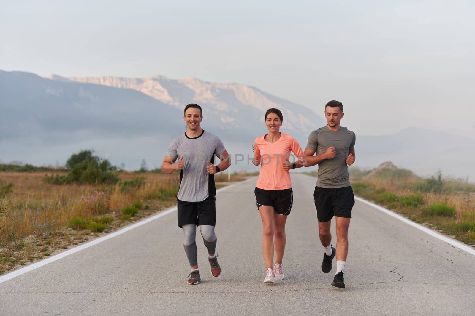 A group of friends, athletes, and joggers embrace the early morning hours as they run through the misty dawn, energized by the rising sun and surrounded by the tranquil beauty of nature.