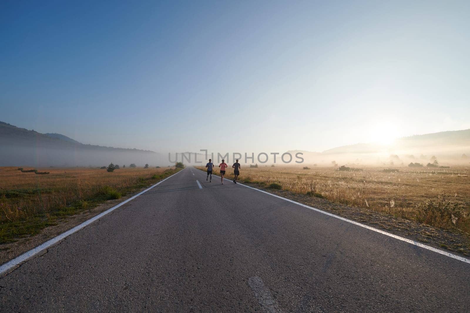 A group of friends, athletes, and joggers embrace the early morning hours as they run through the misty dawn, energized by the rising sun and surrounded by the tranquil beauty of nature.