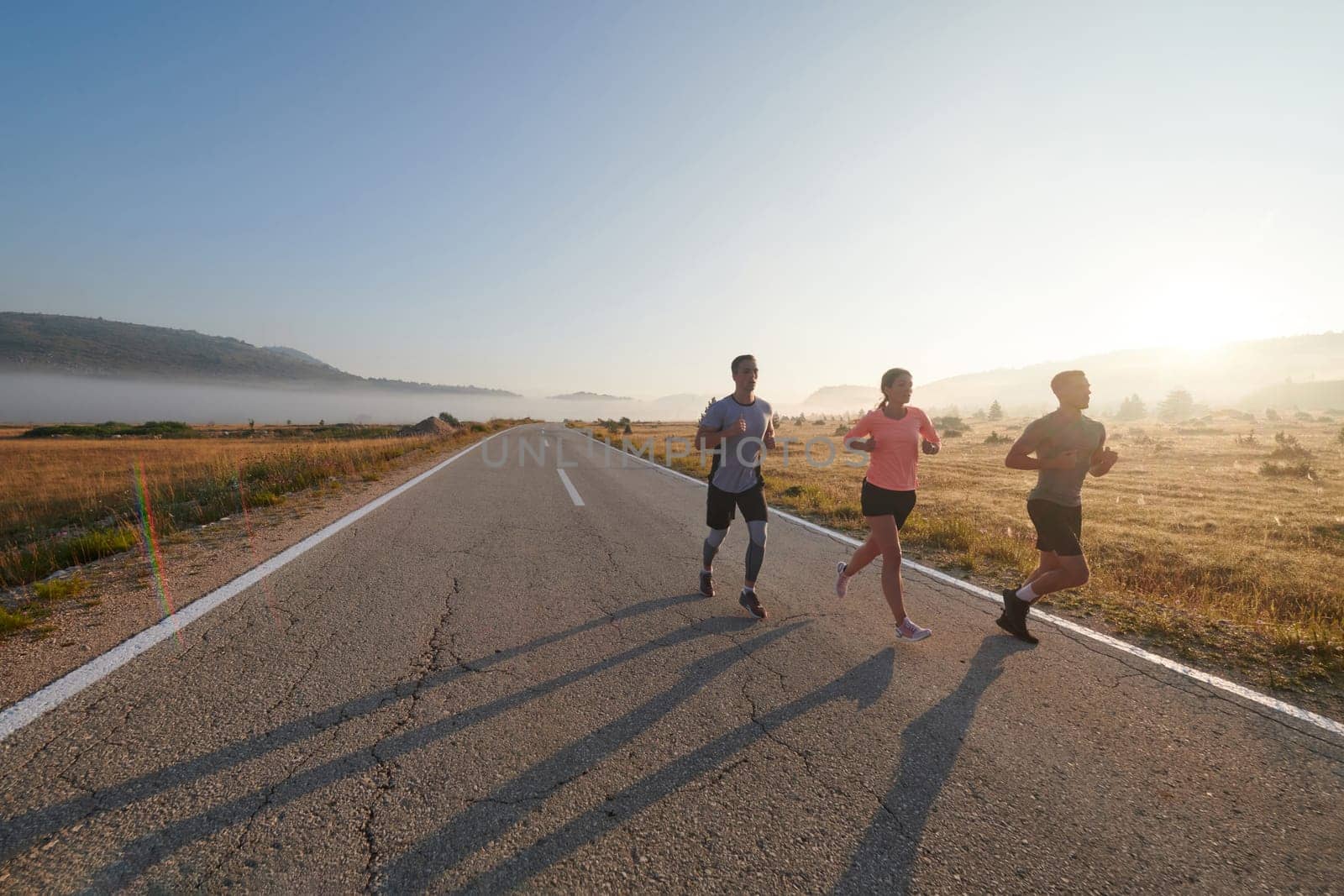 A group of friends, athletes, and joggers embrace the early morning hours as they run through the misty dawn, energized by the rising sun and surrounded by the tranquil beauty of nature.