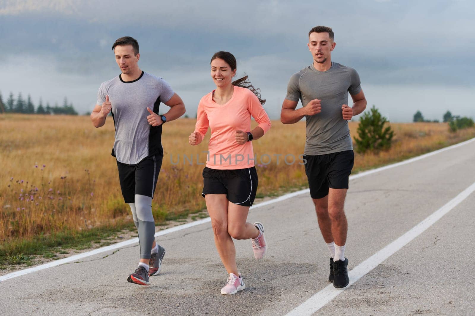 A group of friends, athletes, and joggers embrace the early morning hours as they run through the misty dawn, energized by the rising sun and surrounded by the tranquil beauty of nature.