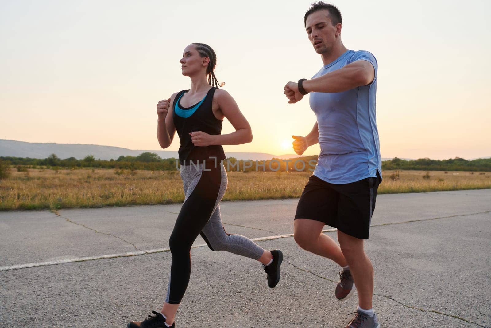 A vibrant couple dashes running the outdoors, embodying the essence of athleticism and romance, their confident strides reflecting a shared commitment to fitness and preparation for future marathon challenges.