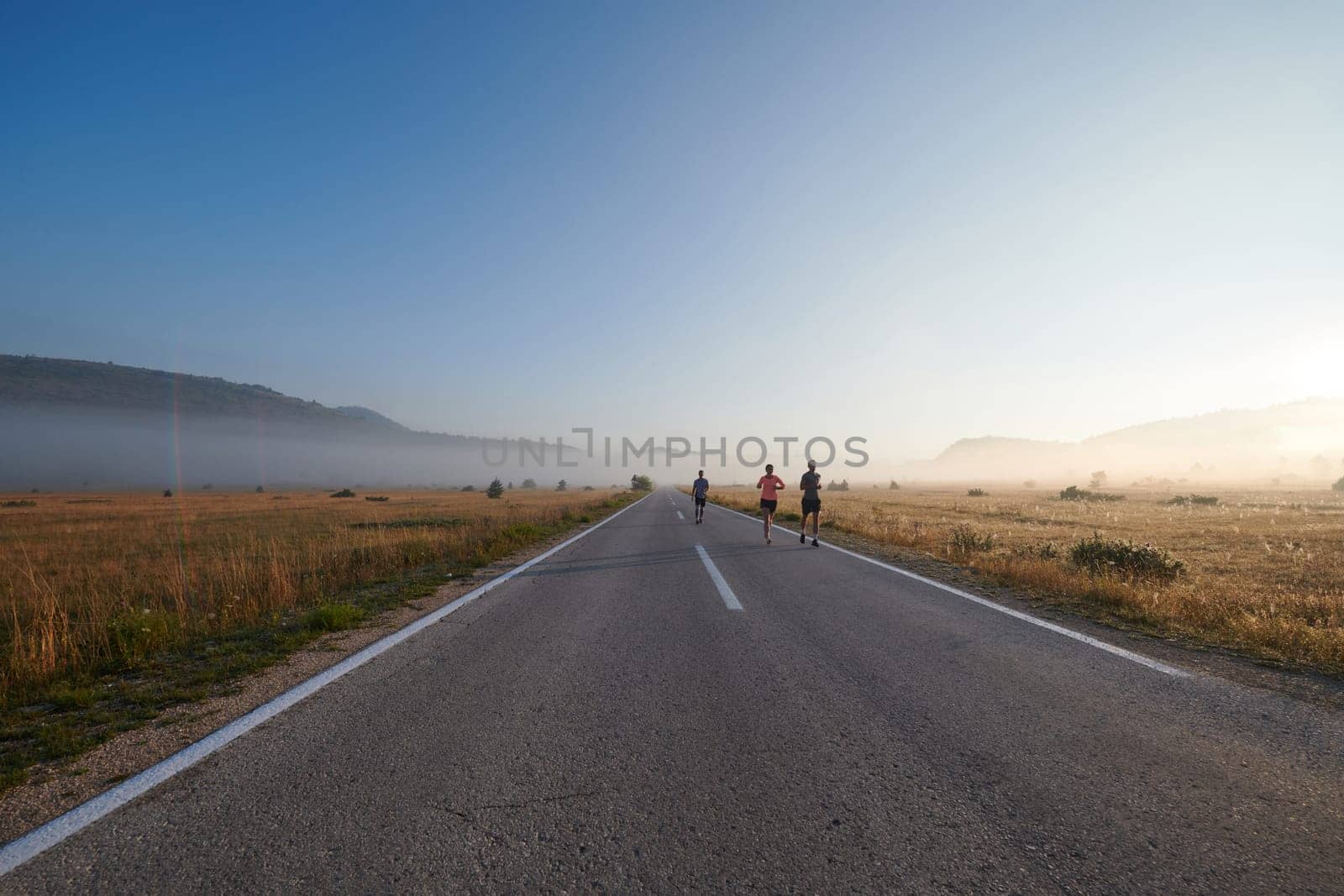 A group of friends, athletes, and joggers embrace the early morning hours as they run through the misty dawn, energized by the rising sun and surrounded by the tranquil beauty of nature.