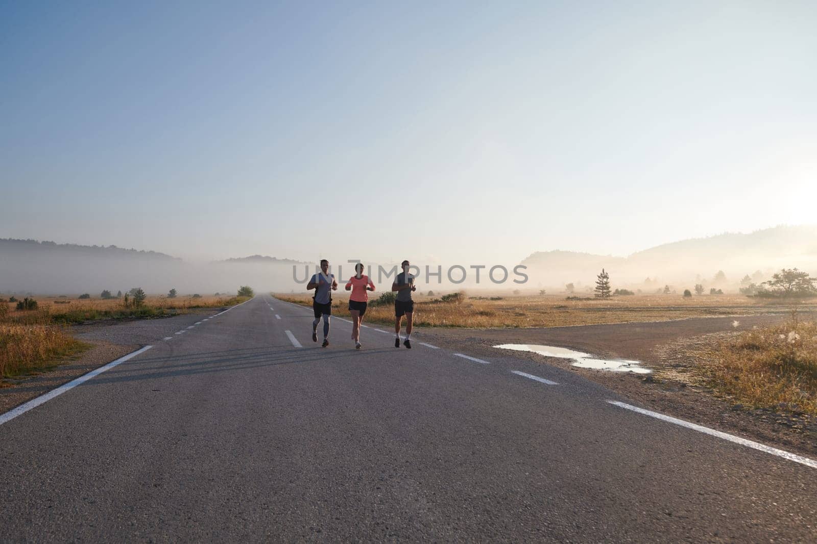 A group of friends, athletes, and joggers embrace the early morning hours as they run through the misty dawn, energized by the rising sun and surrounded by the tranquil beauty of nature.